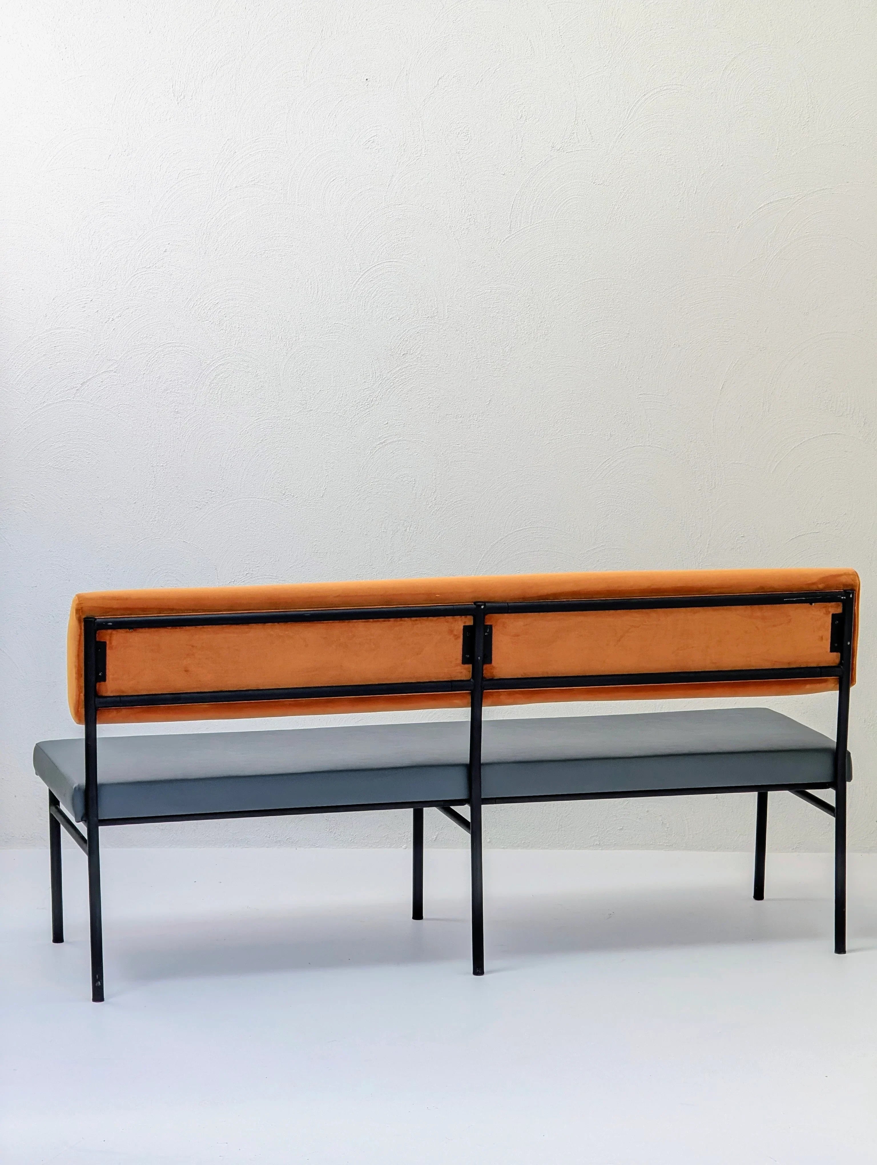 Modern bench with orange backrest, gray seat, and black metal frame against white wall