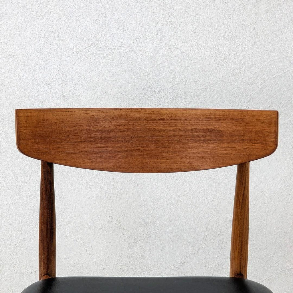 Teak mid-century modern dining chair with black seat against a white textured wall