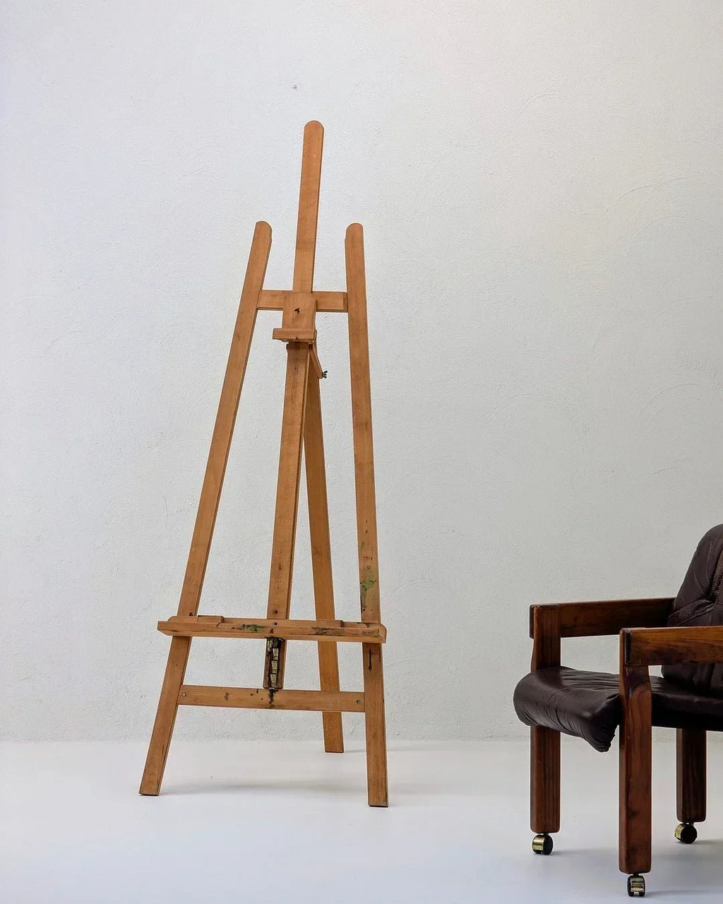 Wooden studio easel by Mabef Italy next to a brown leather chair against a white wall