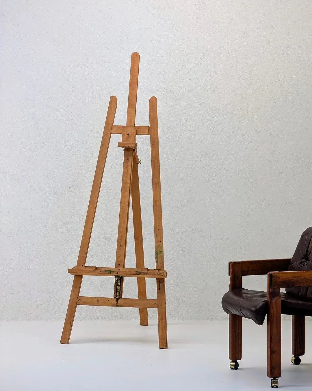 Wooden studio easel by Mabef Italy next to a brown leather chair against a white wall