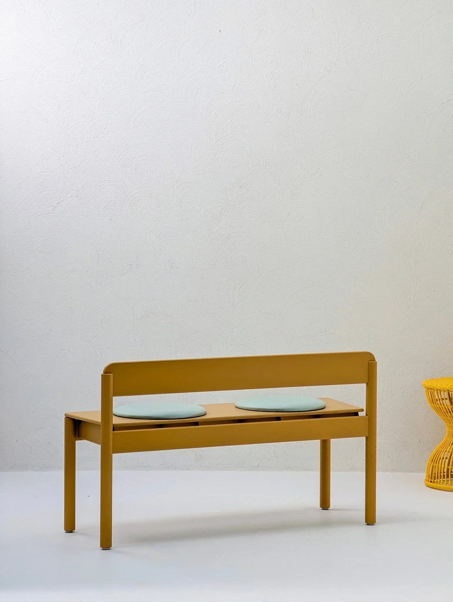 Modern mustard yellow bench with pale seat cushions beside sculptural yellow woven stool