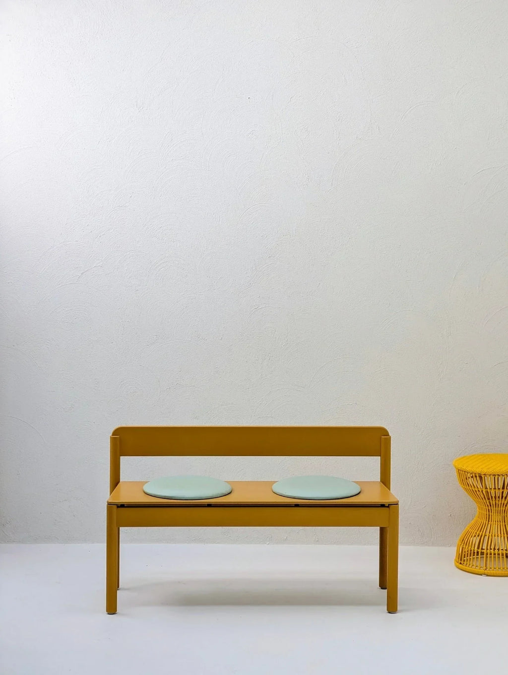 Yellow sculptural woven stool and modern yellow bench with round blue cushions in minimal room