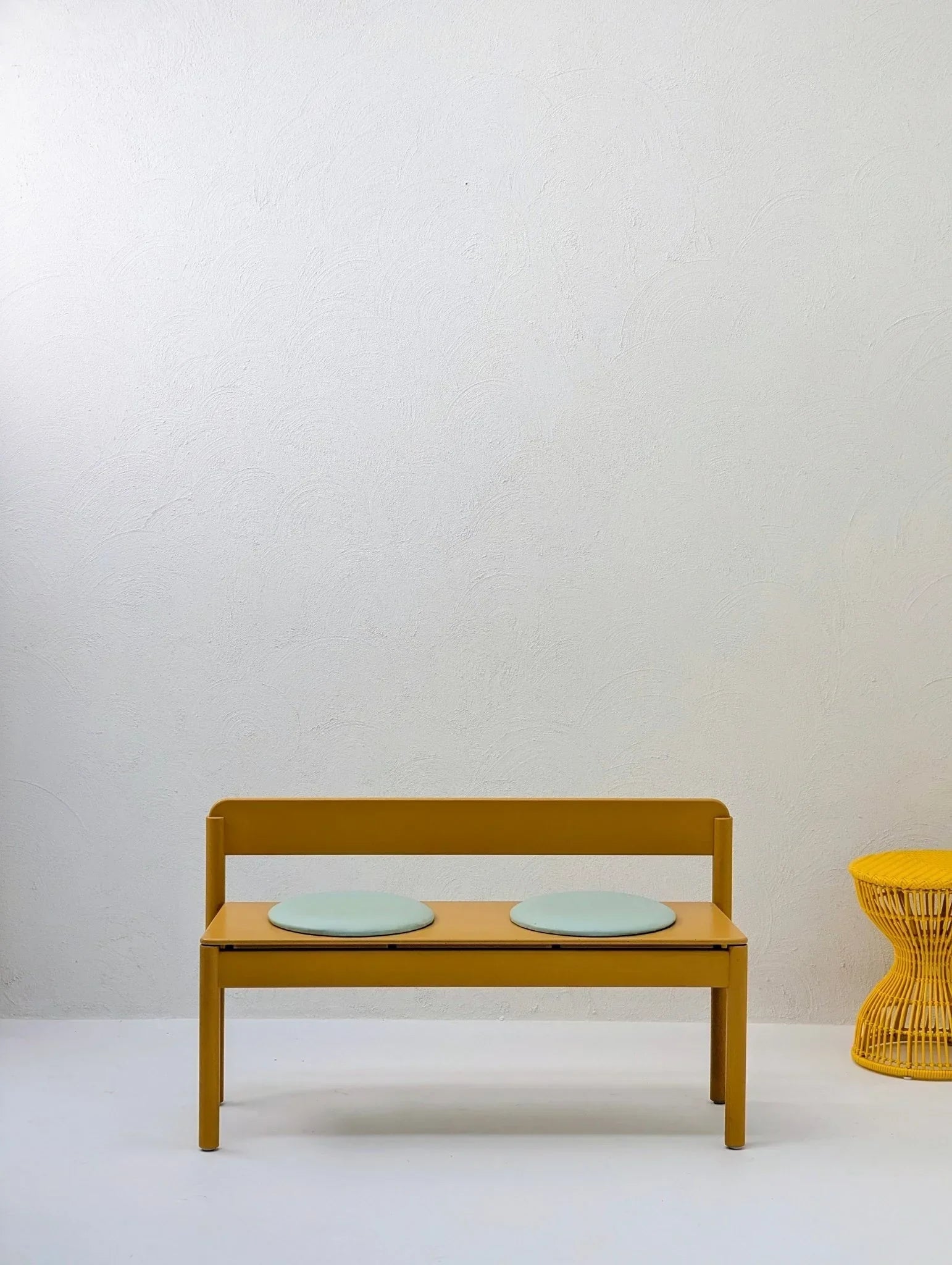 Yellow sculptural woven stool and modern yellow bench with round blue cushions in minimal room