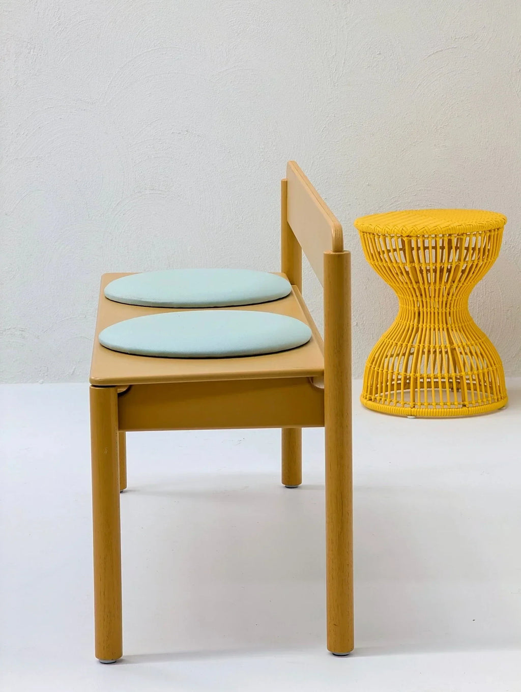 Yellow sculptural woven stool next to minimalist wooden bench with blue cushions