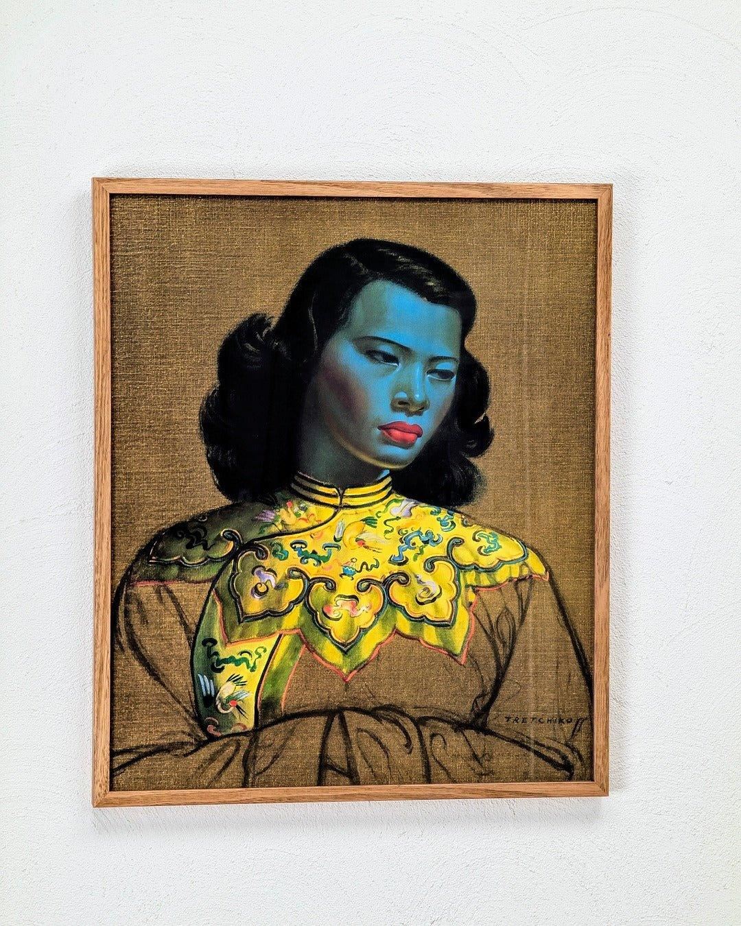 Vintage print of woman with blue skin in ornate yellow dress, framed against neutral wall