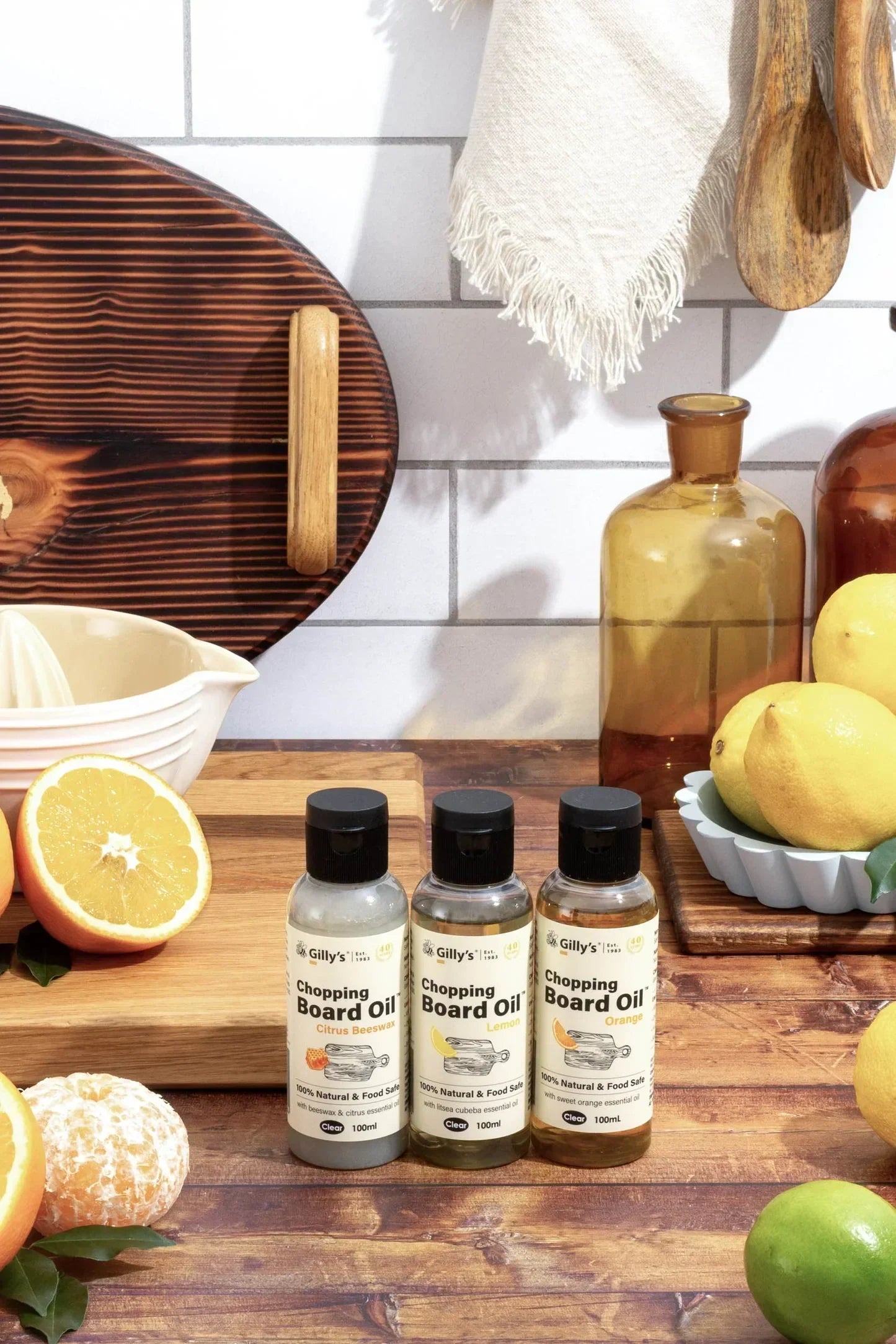 Three Gilly's Chopping Board Oil bottles with citrus fruits on wooden kitchen counter