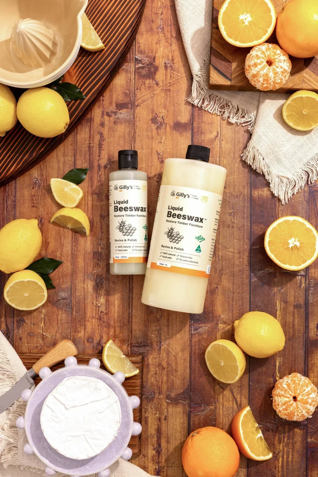 Gilly's Liquid Beeswax bottles on wooden table with lemons, oranges, and cheese