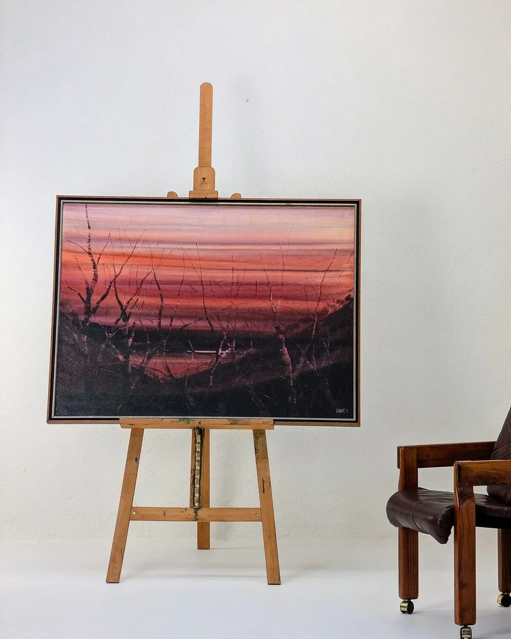 Vintage framed oil painting of abstract sunset on easel beside brown leather chair