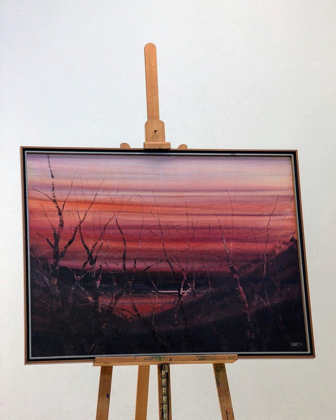 Vintage framed oil painting of a sunset landscape with bare trees on an easel