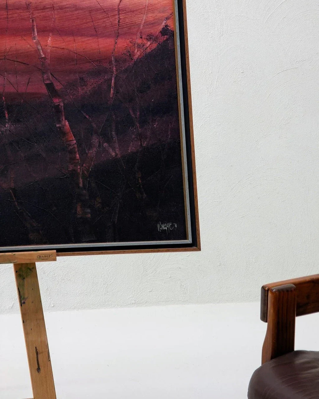 Vintage framed oil painting of a dark landscape with red sky, on easel, near wooden chair
