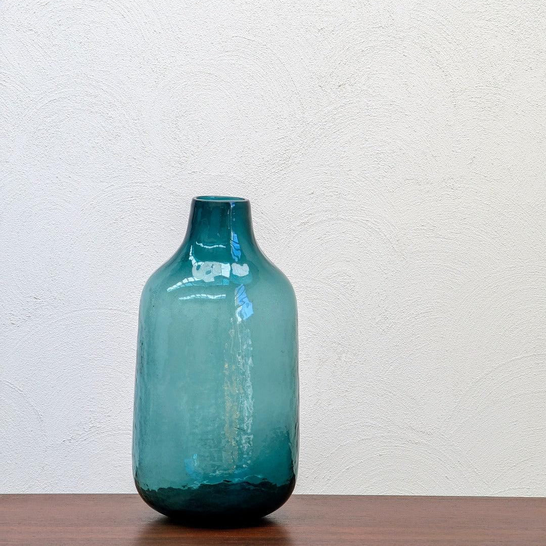 Vintage teal art glass vase on wooden table against white textured wall
