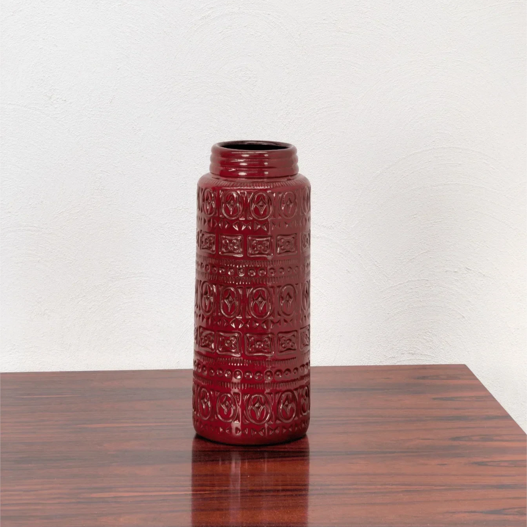 Tall deep red West German mid-century modern vase with embossed geometric patterns on wooden table
